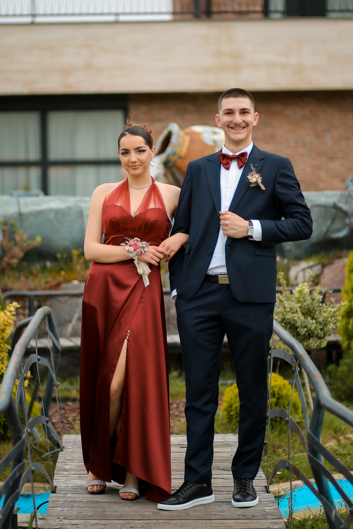 services-03 A well-dressed couple stands confidently on a footbridge, showcasing formalwear in an outdoor setting.